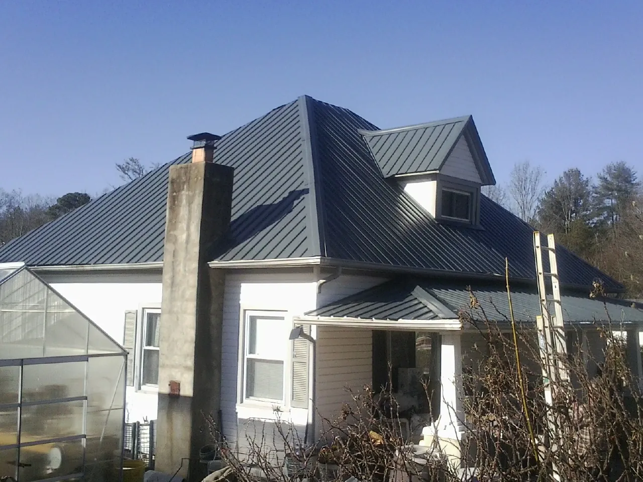 Dark blue standing seam metal roof on a white farmhouse with dormer — Slate & Tile Roof Repair by Roofing Brothers in Syosset