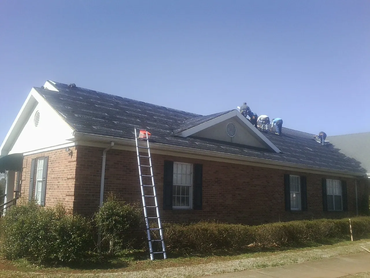 Crew tearing shingles off a brick ranch roof with a ladder set — Metal Roof Repair work by our crew in Syosset