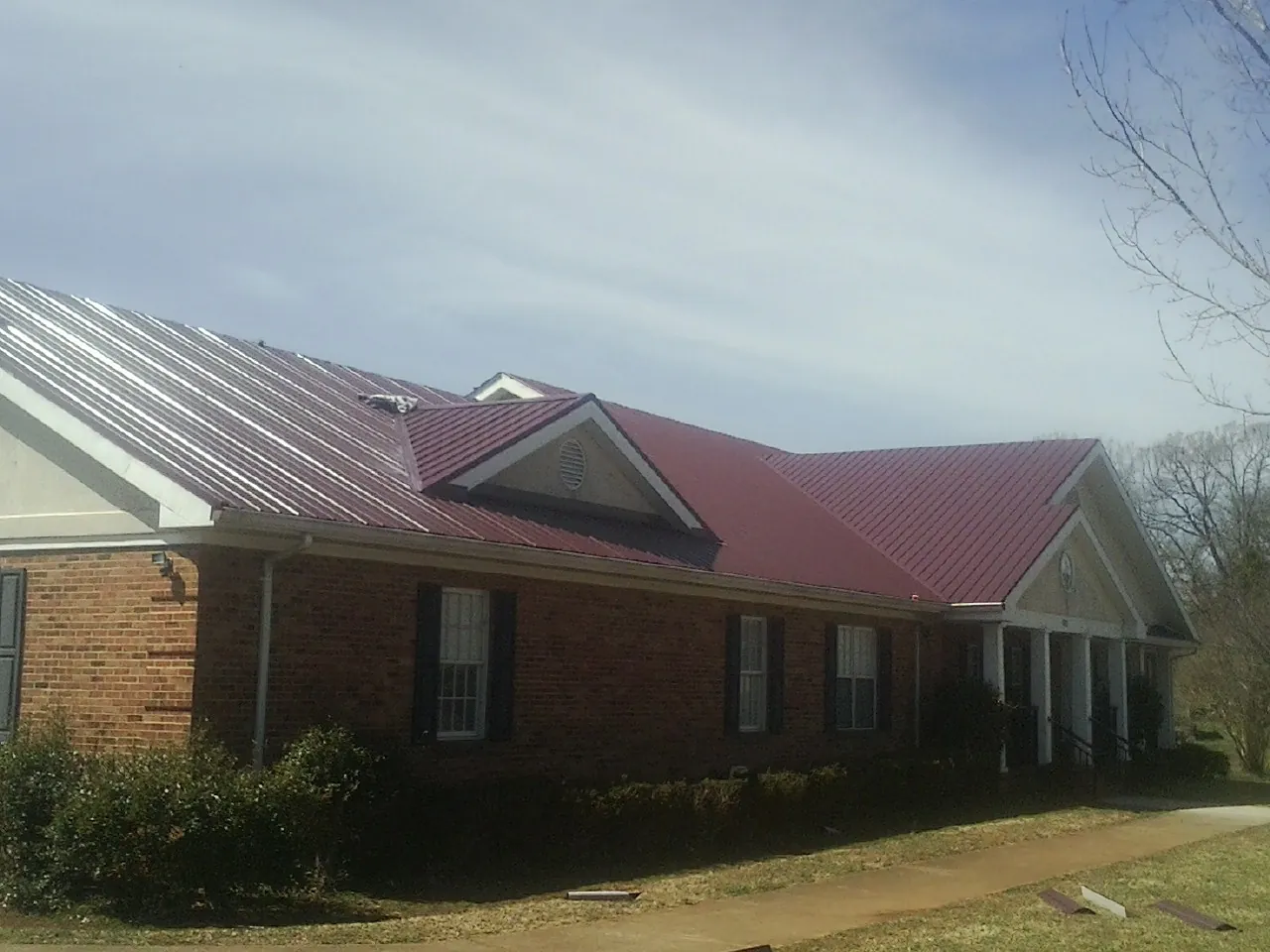 Red metal roof with gabled entries on a long brick building, from a Hail Damage Roof Repair job in Syosset