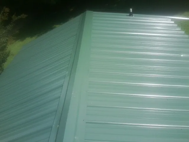 New green metal panels meeting at the ridge of a roof — Flat Roof Repair work by our crew in Syosset