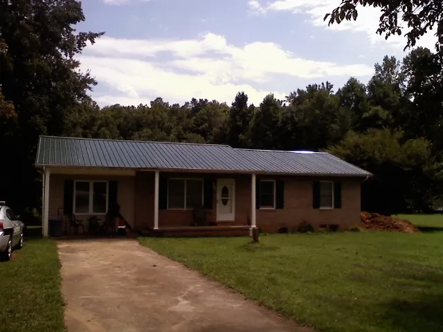 Dark green metal roof on a brick ranch with a covered porch in Syosset