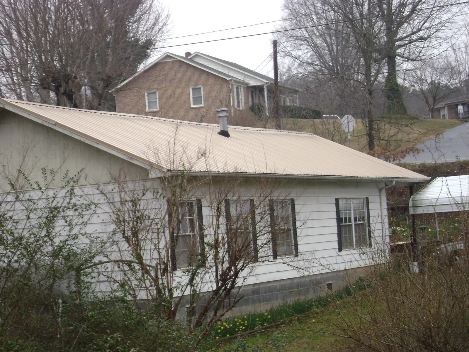 Tan metal roof on a white sided house set into a hillside — Commercial Roofing by Roofing Brothers in Syosset